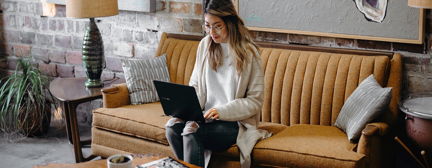 young woman sits on a cafe couch while working on her laptops
