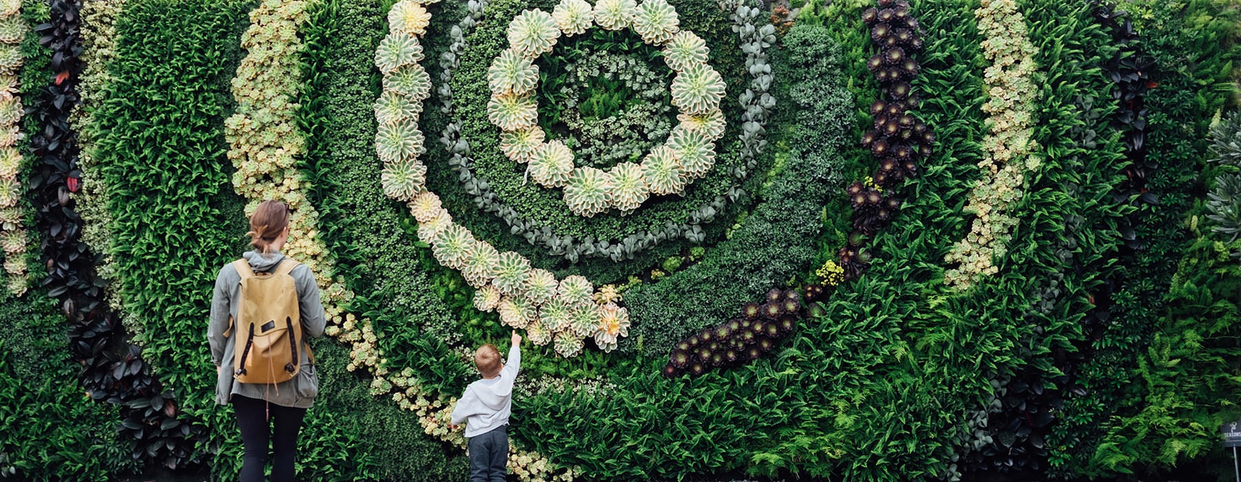 mother and son stand in front of a large wall of plants in circular design