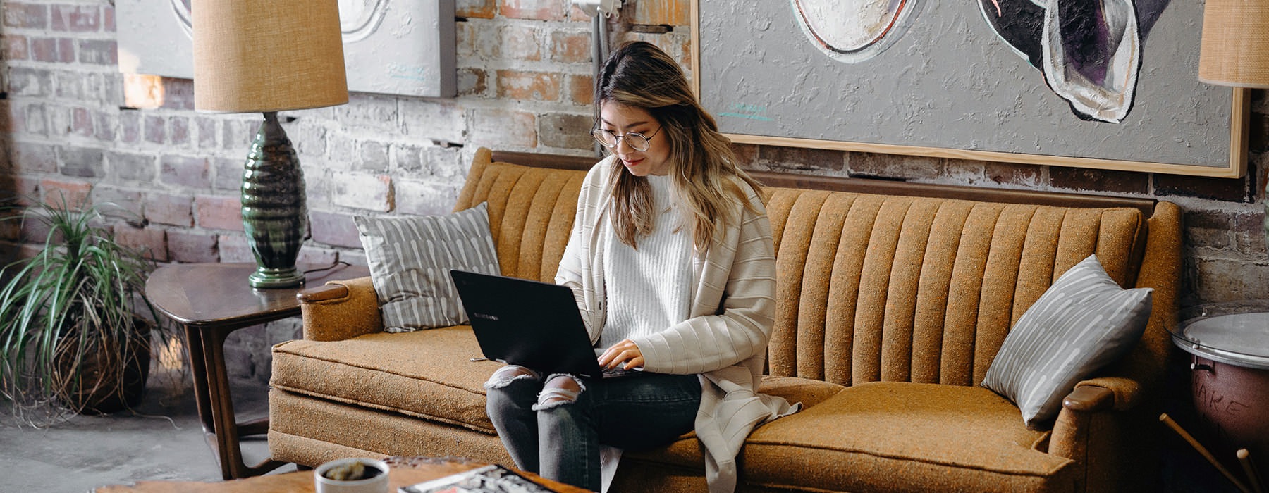 young woman sits on a cafe couch while working on her laptops